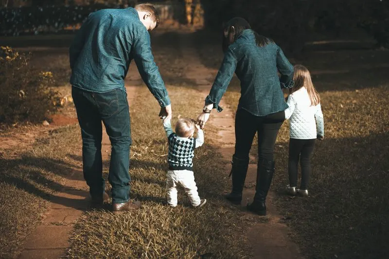 Two parents walking hand in hand with two young children on a dirt path
