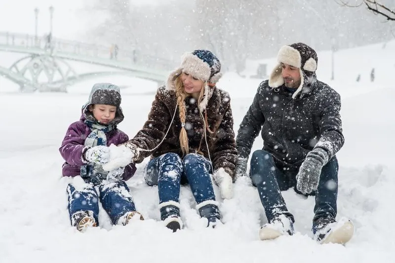 Family in winter coats sitting together in the snow
