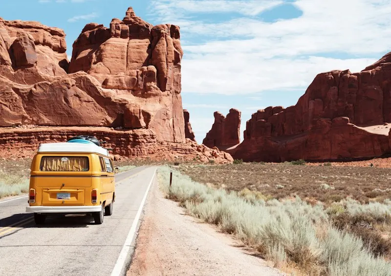 Yellow van on a desert road past red rock formations