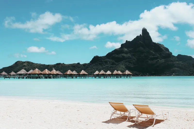 Tropical beach with overwater bungalows and two lounge chairs