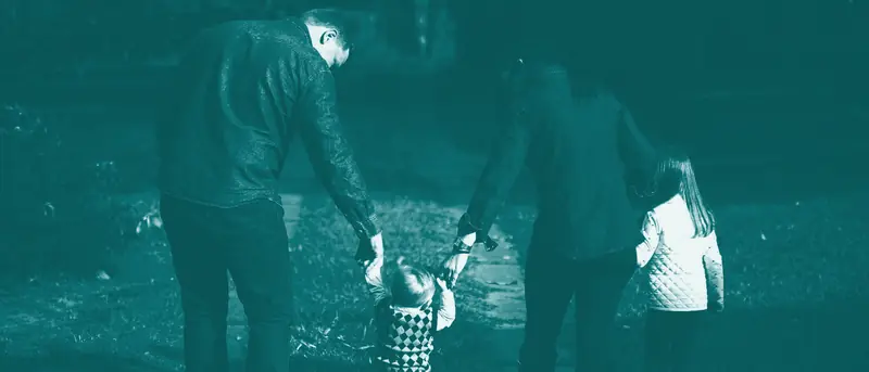 Two parents walking hand in hand with two young children on a path, in PointFam teal
